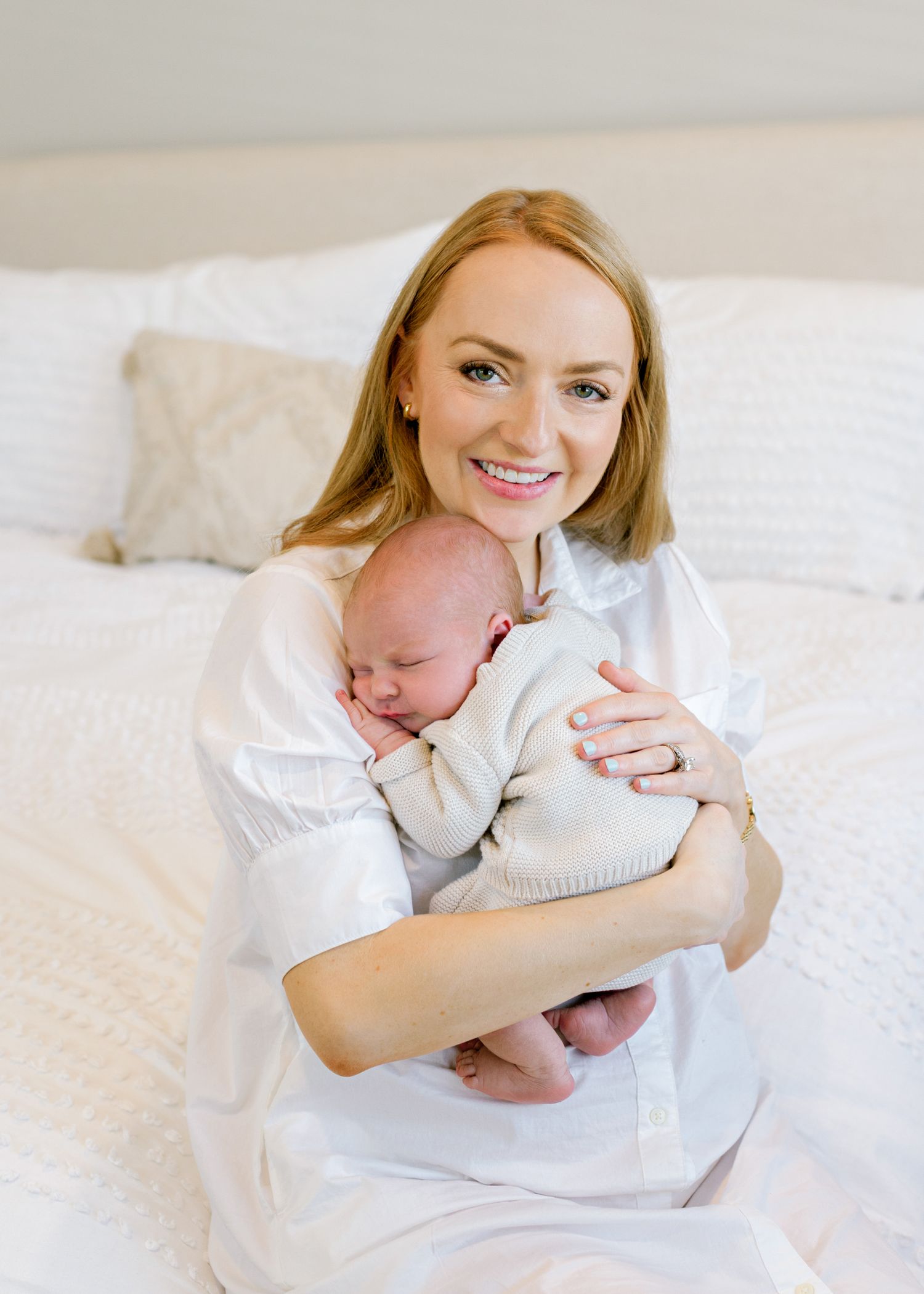 Sweet lifestyle newborn portrait with white clothing and neutral bedding in bright natural light.
