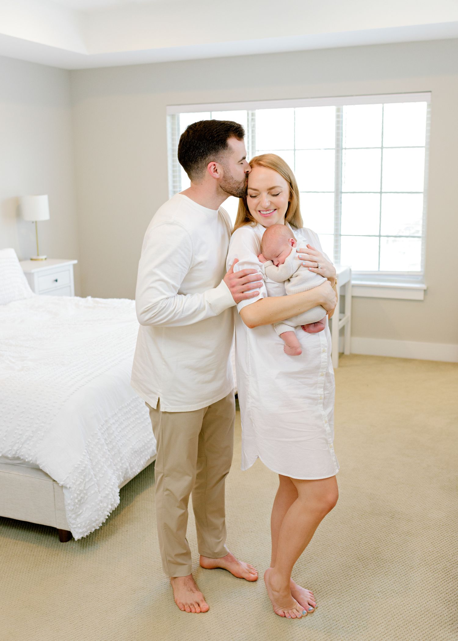 Light and airy lifestyle portrait of a family with newborn in a bright modern bedroom.