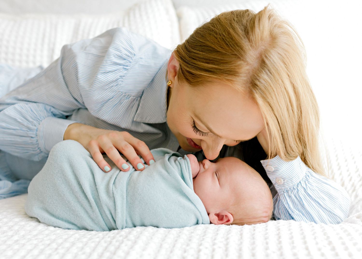 Intimate mother and baby portrait on white bedding with soft natural lighting.