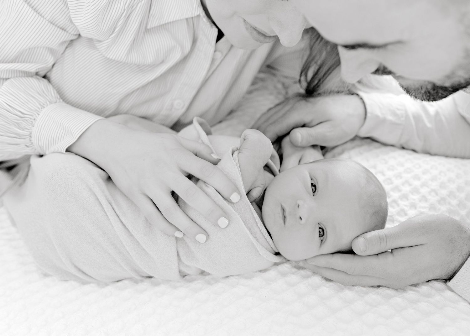 Black and white intimate portrait of parent and baby lying together on textured bedding.