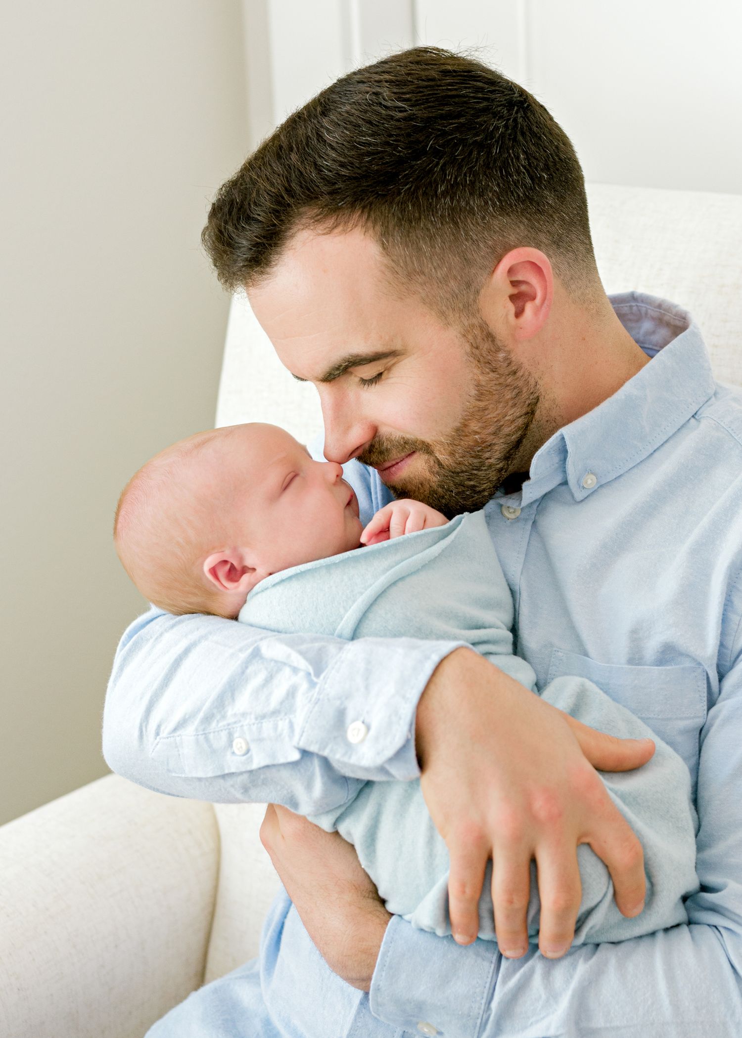 Tender moment between parent and baby dressed in light blue against white background.