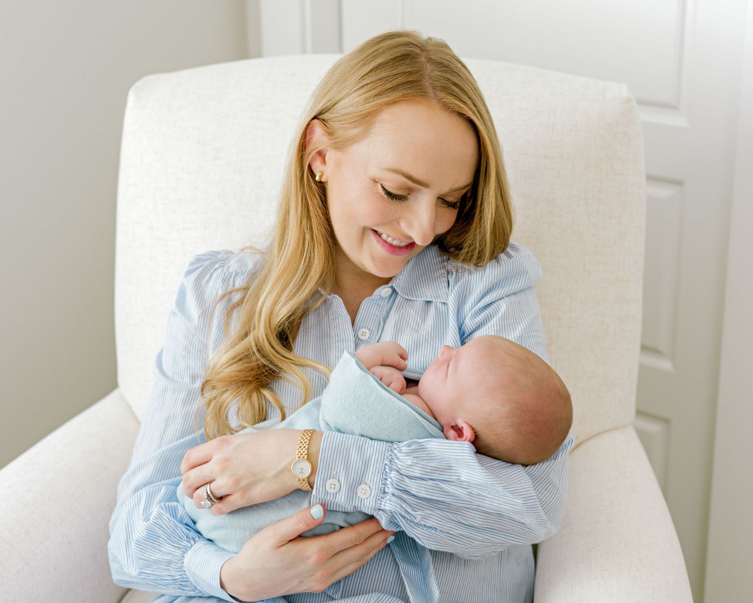 A heartwarming scene of a woman in blue cradling a sleeping newborn baby in white.