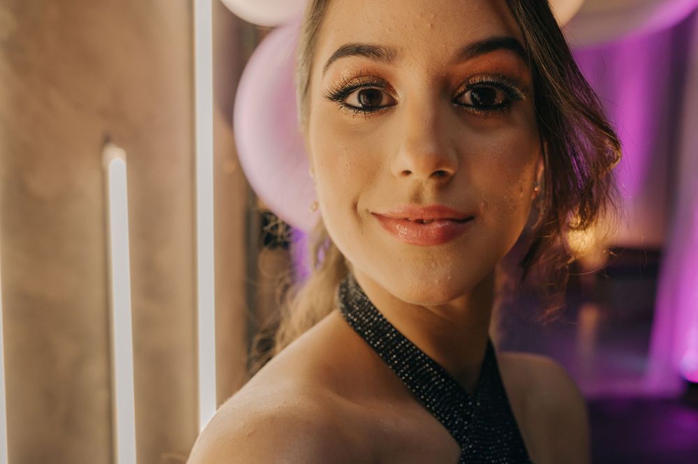 A portrait shot featuring someone in a sparkly halter top against a purple-lit background.