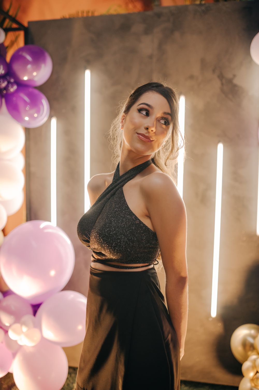 A festive portrait with pink balloons and vertical light strips against a textured wall.