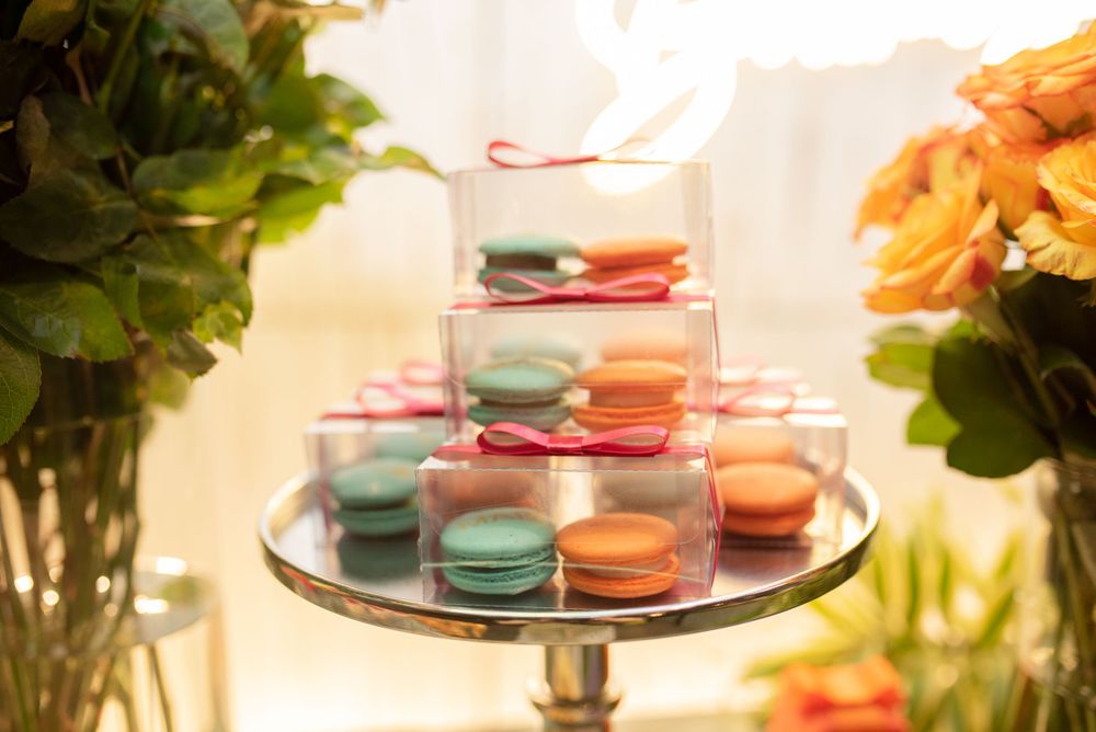Colorful French macarons arranged on a tiered display stand with green plants in the background.