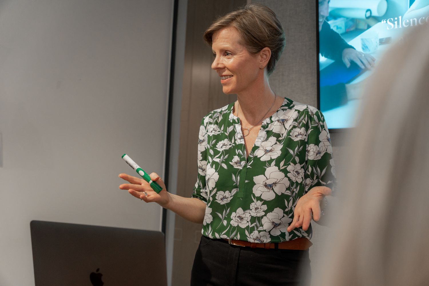 coach woman wearing flowery top is presenting to a group of people in boardroom