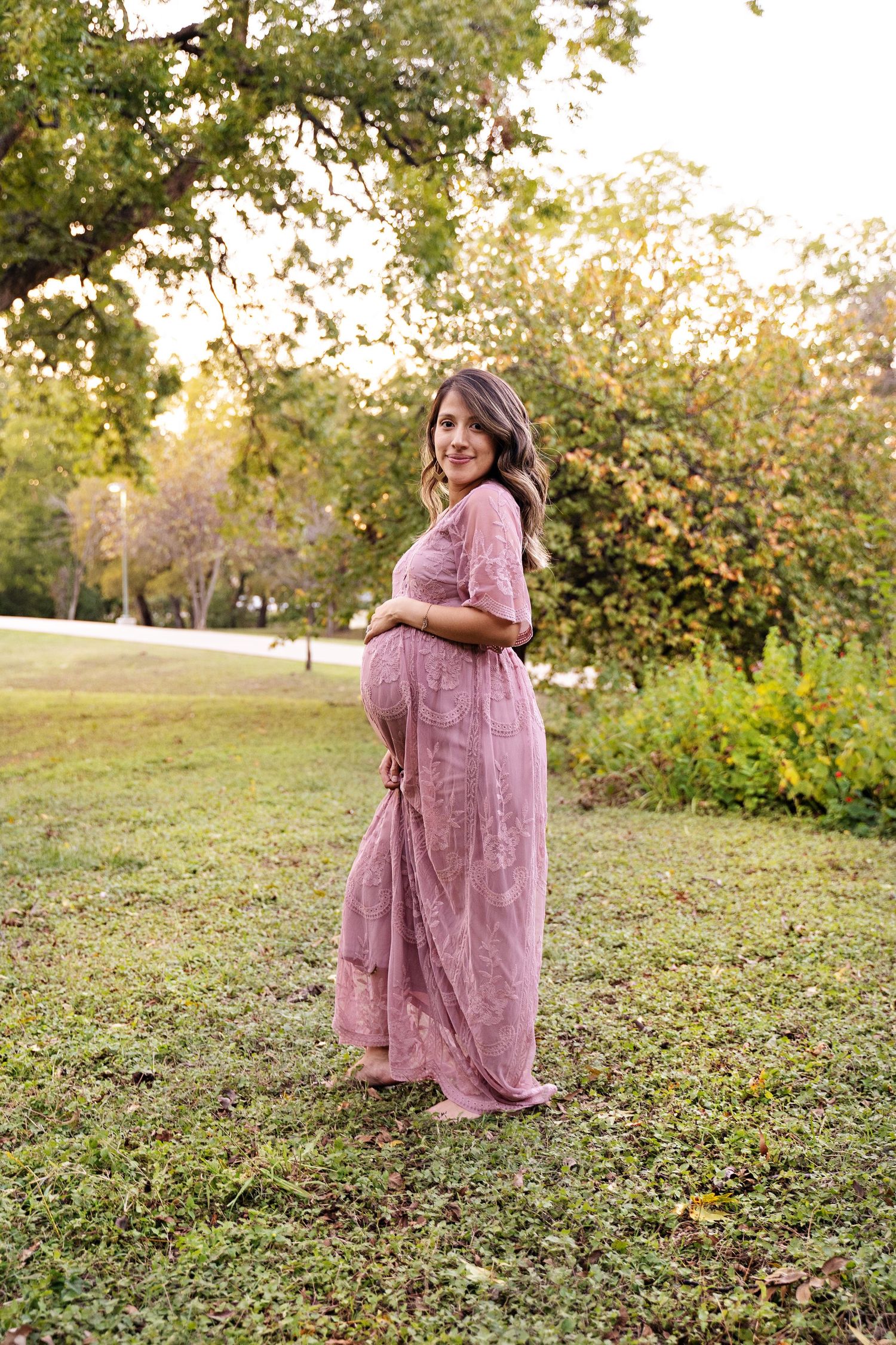 Woman in a flowing pink dress twirls gracefully in a sunlit garden setting during a photo session.