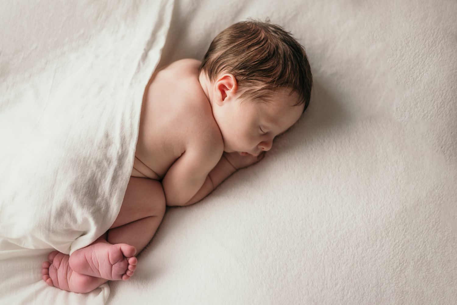 Sleeping newborn baby lying on white blanket during professional photography session.