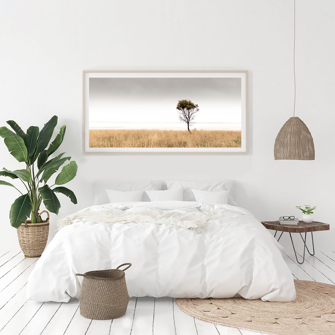 Serene bedroom interior with framed landscape photograph of solitary tree in golden field.