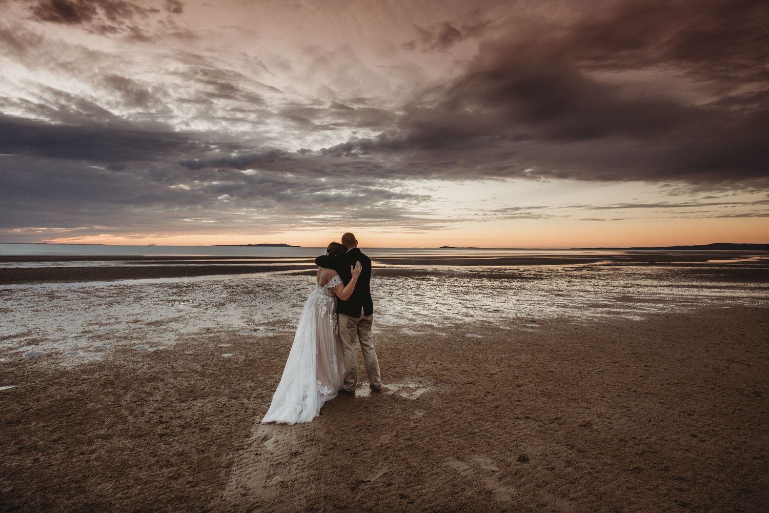 Sunset beach wedding silhouette with dramatic cloudy sky and ocean backdrop.