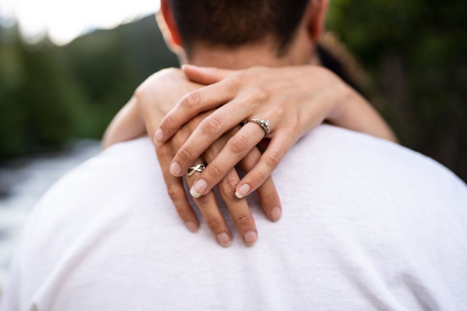 Close-up shot of hands displaying an engagement ring against a white shirt.