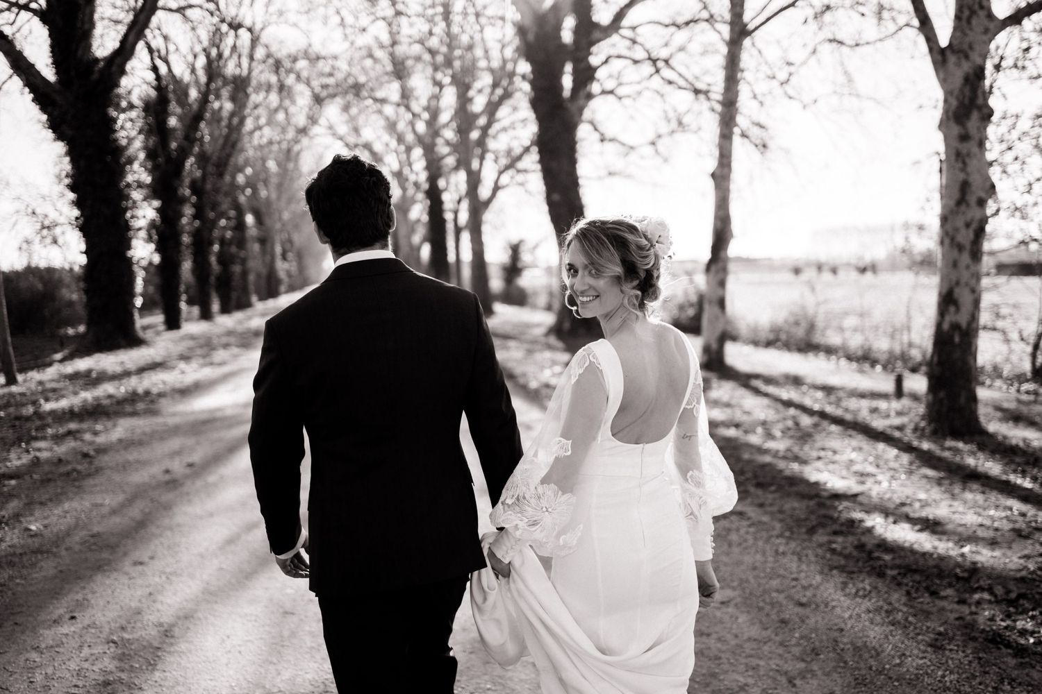Newlyweds walking down a countryside road surrounded by trees in black and white.