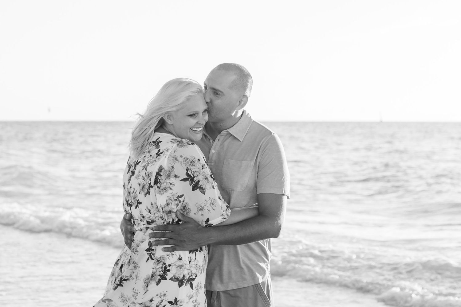 Black and white photo of couple sharing intimate moments on a beach.