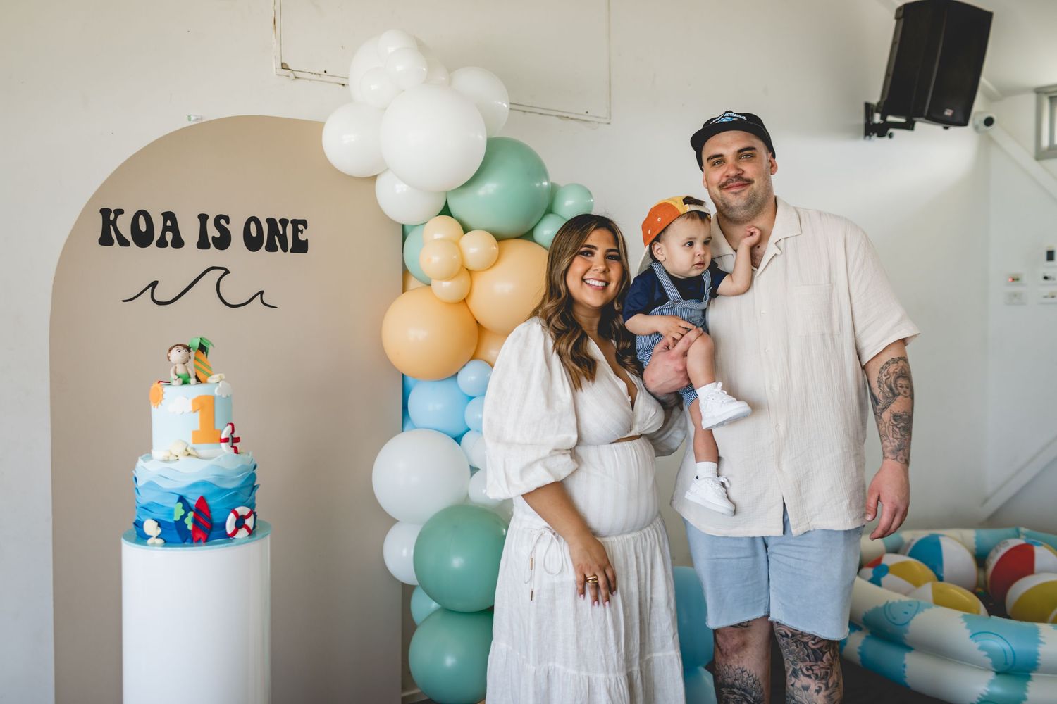 Beach-themed first birthday party setup with balloon arch and decorated cake display.