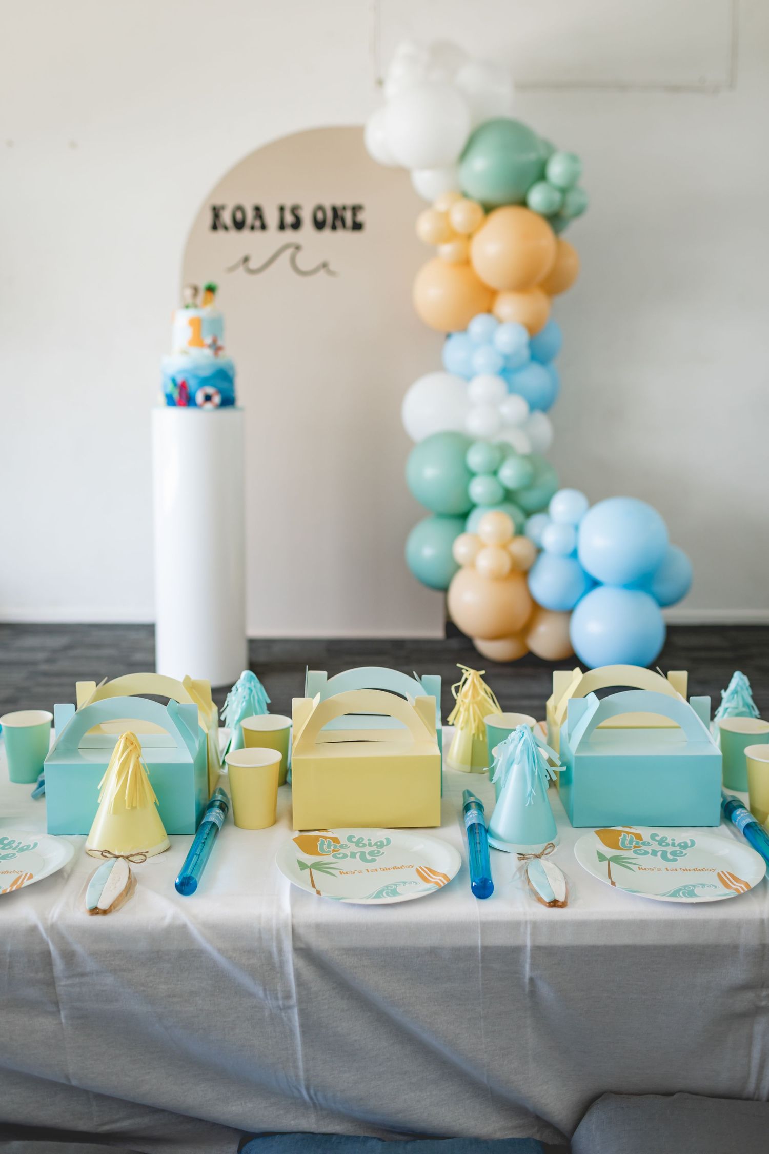 Beach themed party table with mint green favor boxes and pastel balloon decorations.