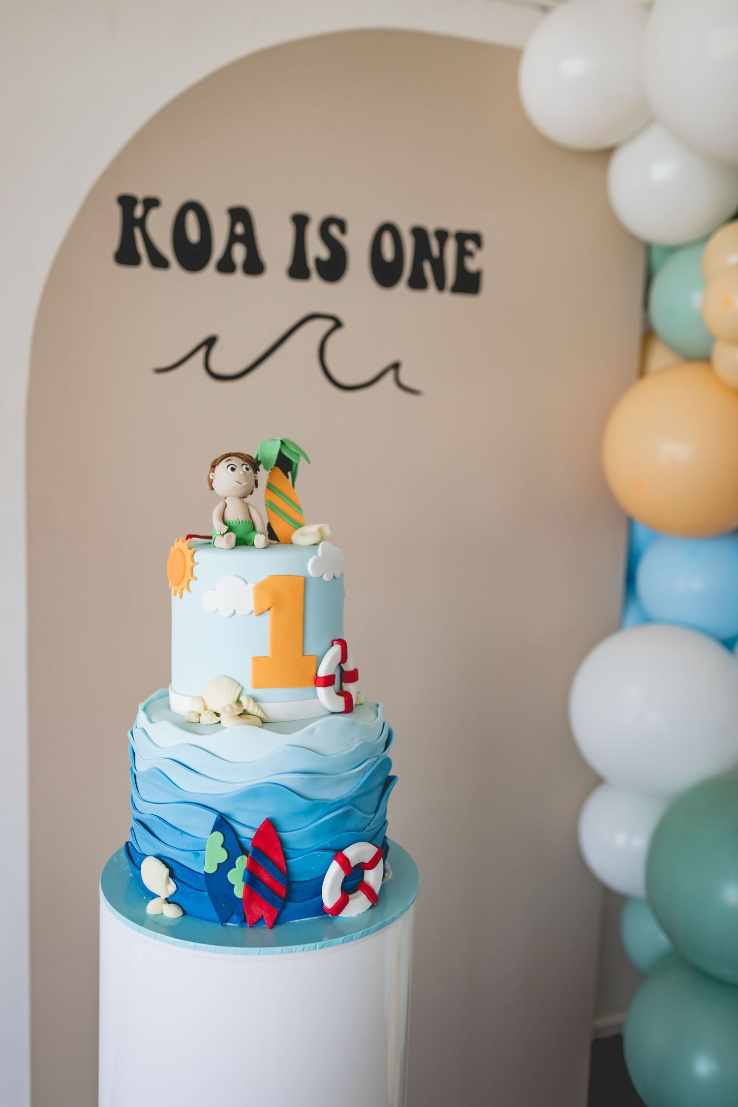 Two-tiered nautical birthday cake with waves and lifesaver decorations on white pedestal.