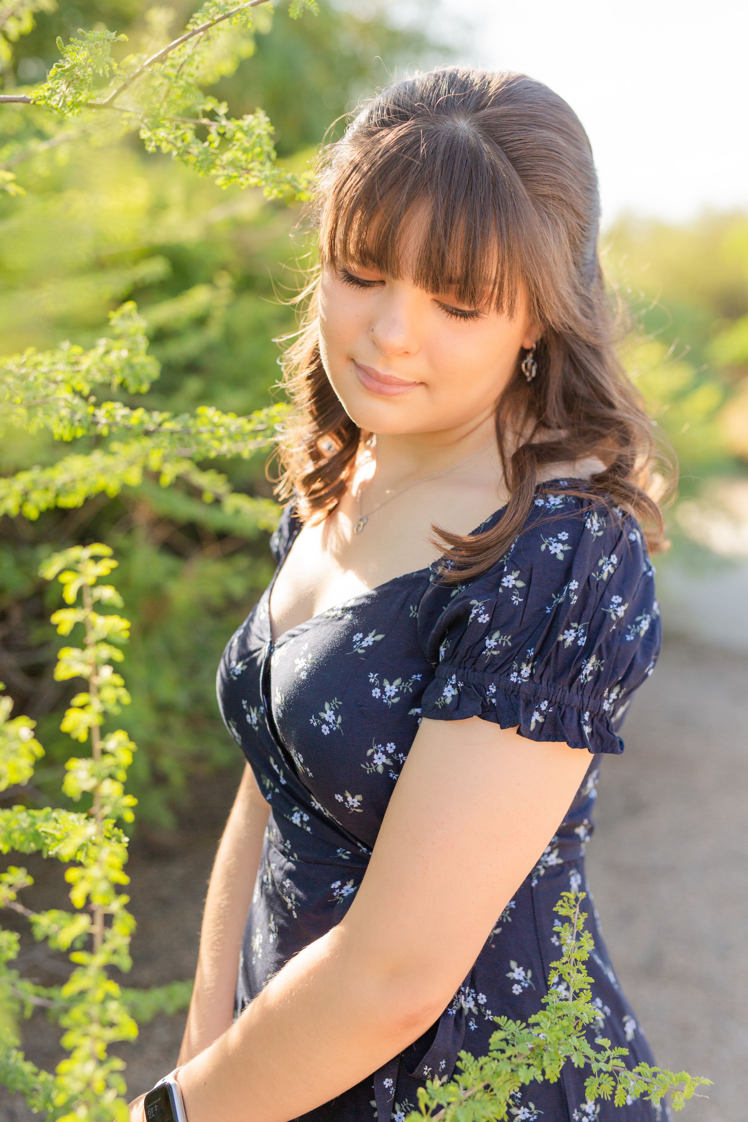 Outdoor portrait in navy floral dress with greenery in background.