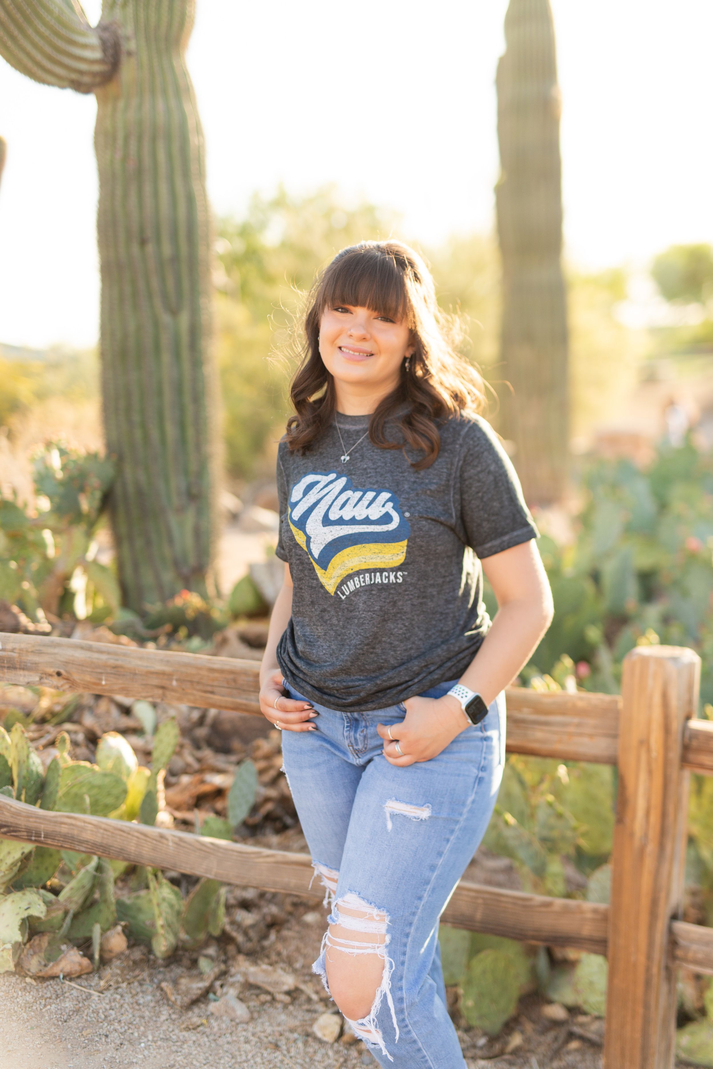 Casual portrait by desert cacti wearing NAU shirt and distressed jeans.