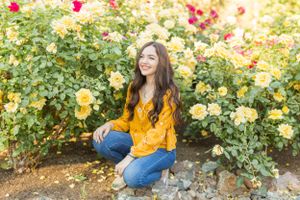 Yellow and red roses bloom in a garden with someone wearing a mustard sweater.