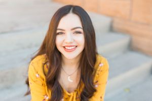Portrait in yellow top against concrete background with bright smile.
