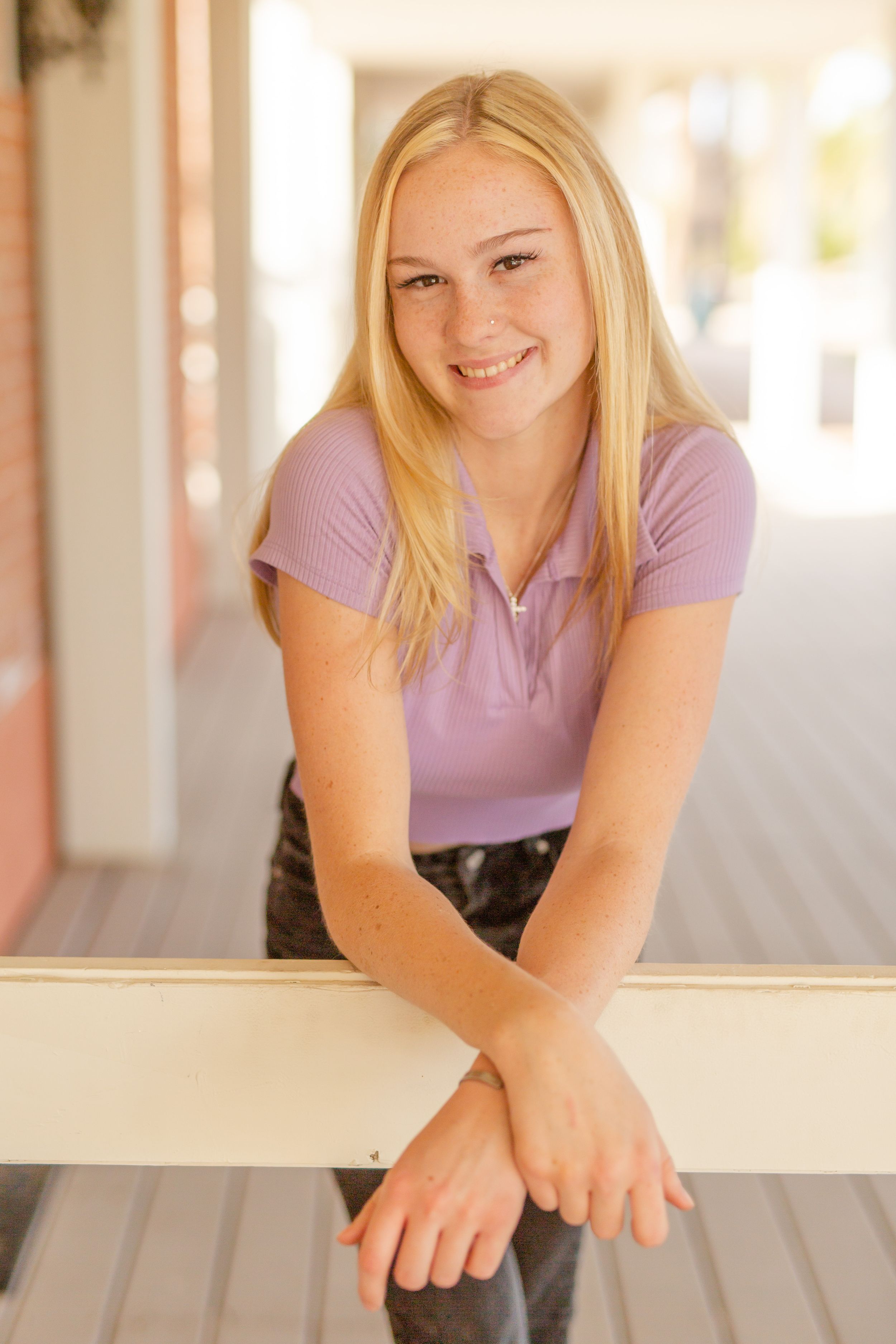 Young person in purple shirt leaning against white railing with a warm smile.
