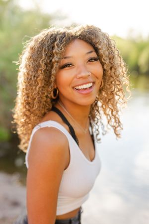 Close-up portrait with curly hair and bright smile outdoors.