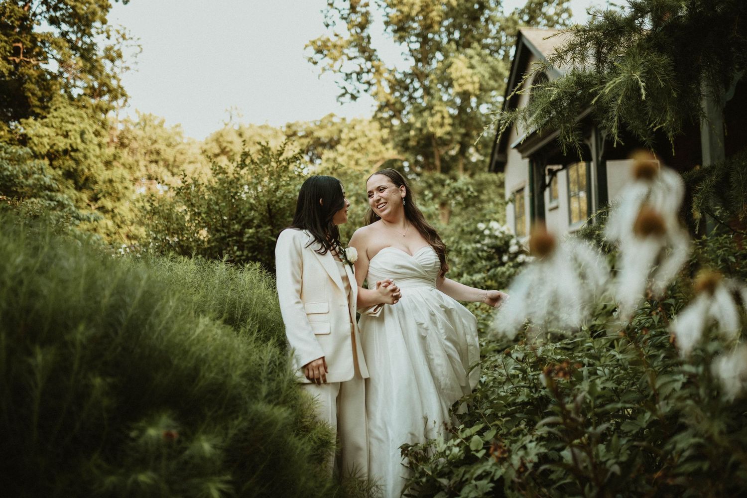 Wedding ceremony setup in a lush garden setting with white chairs and floral arrangements.