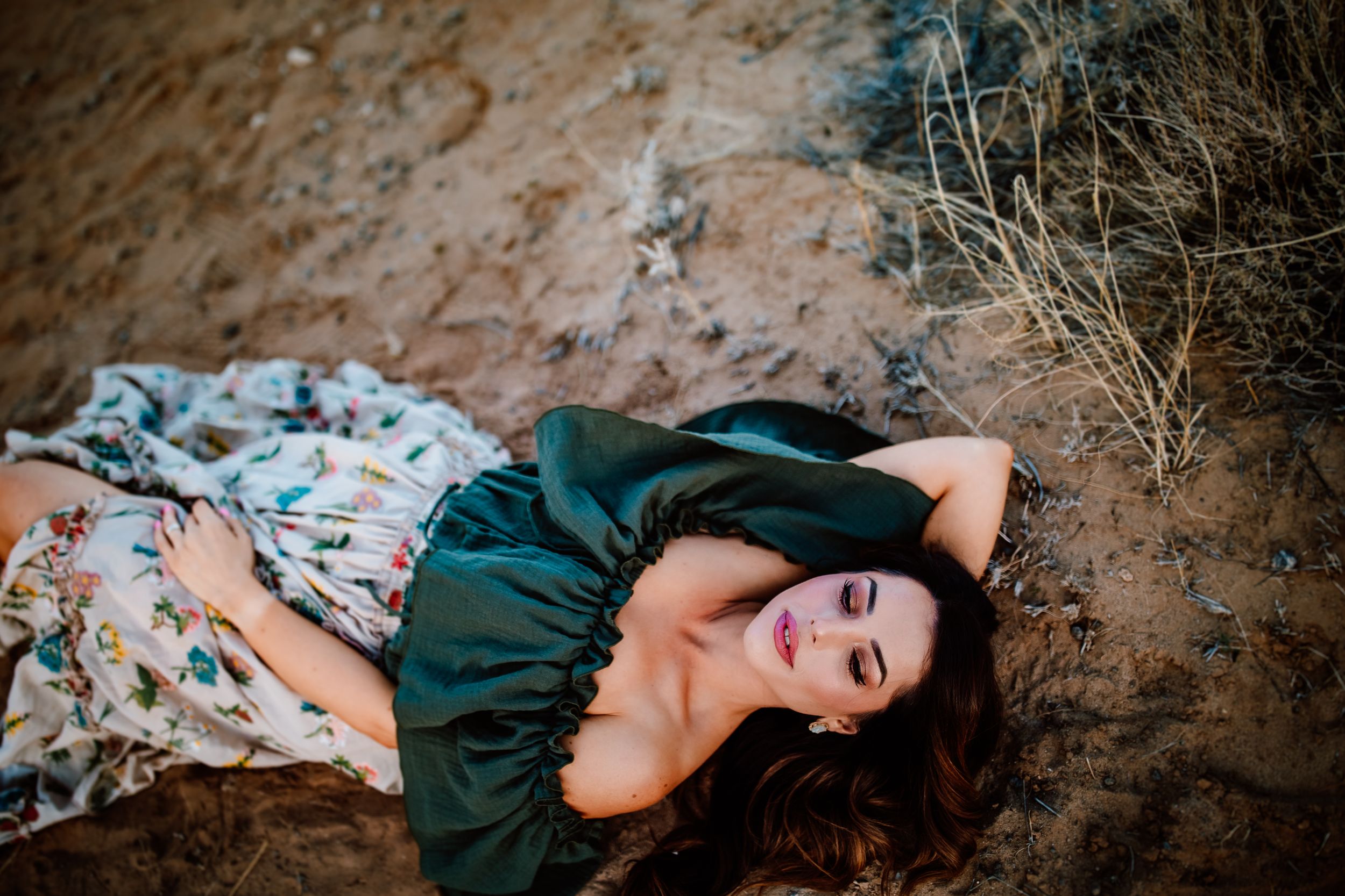 Artistic outdoor portrait with figure lying on red desert rocks wearing a green dress.