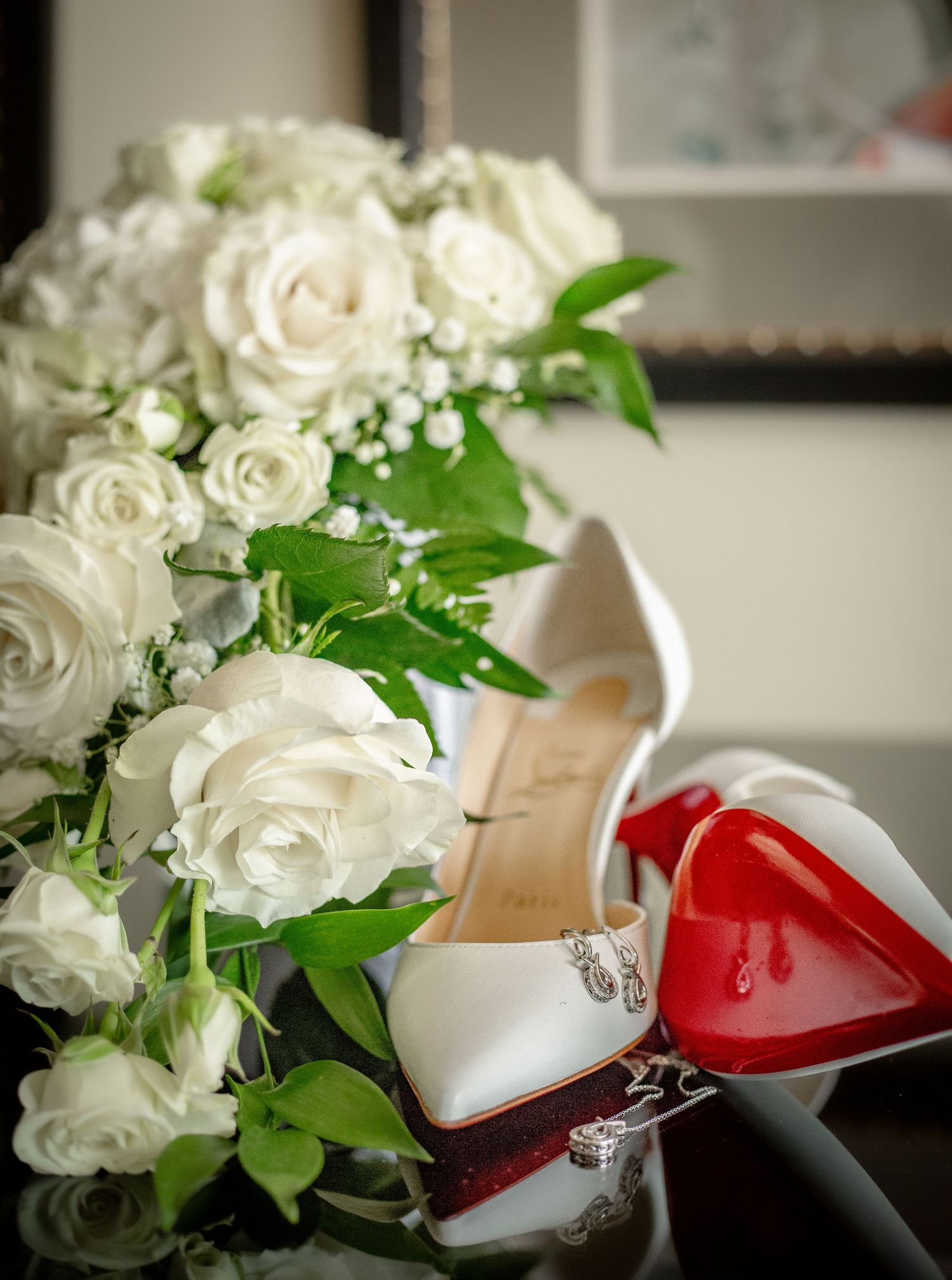 A white rose wedding bouquet pictured with a pair of white Louboutin shoes and bridal jewelry