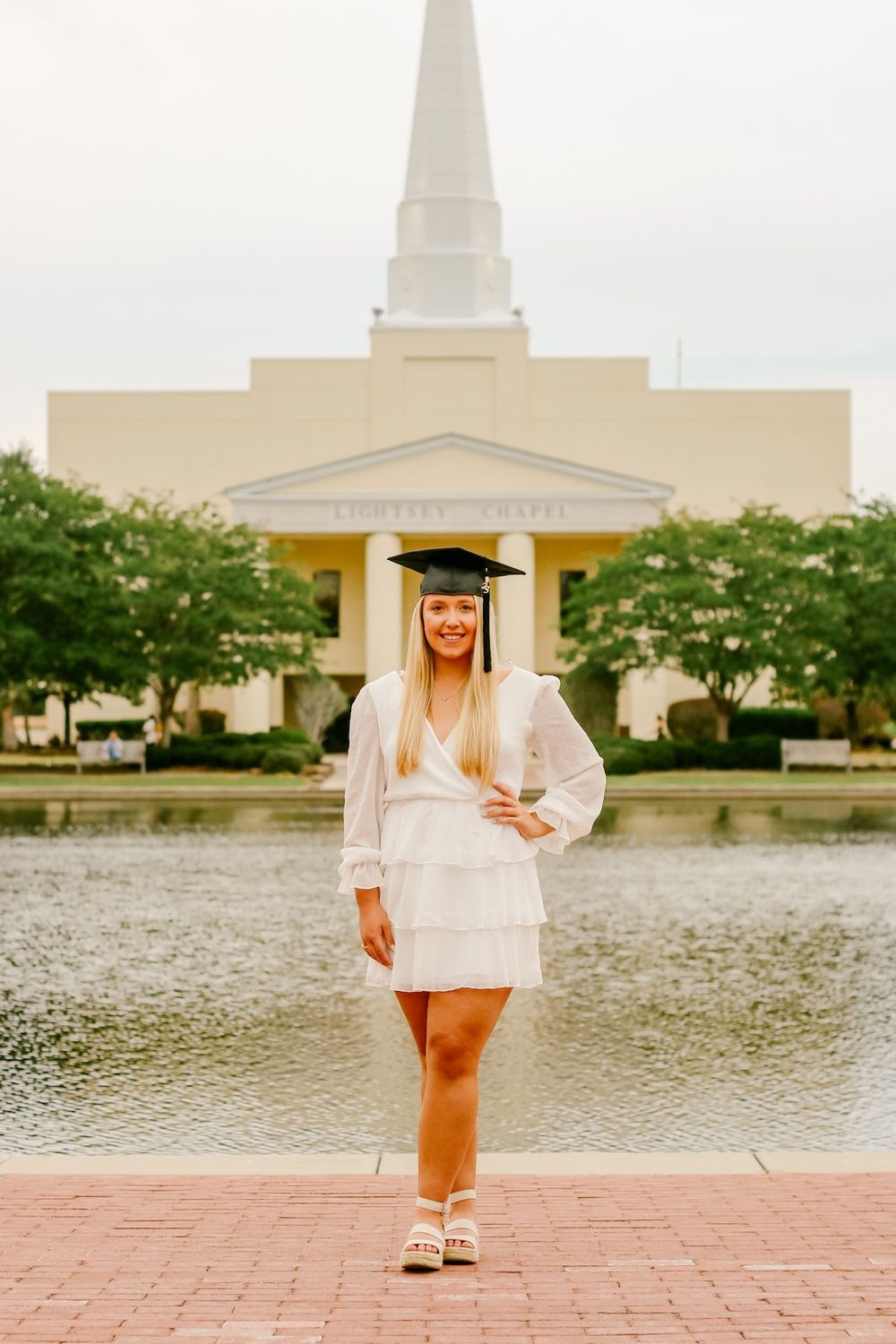 White graduation attire photographed in front of a church with reflecting pool.