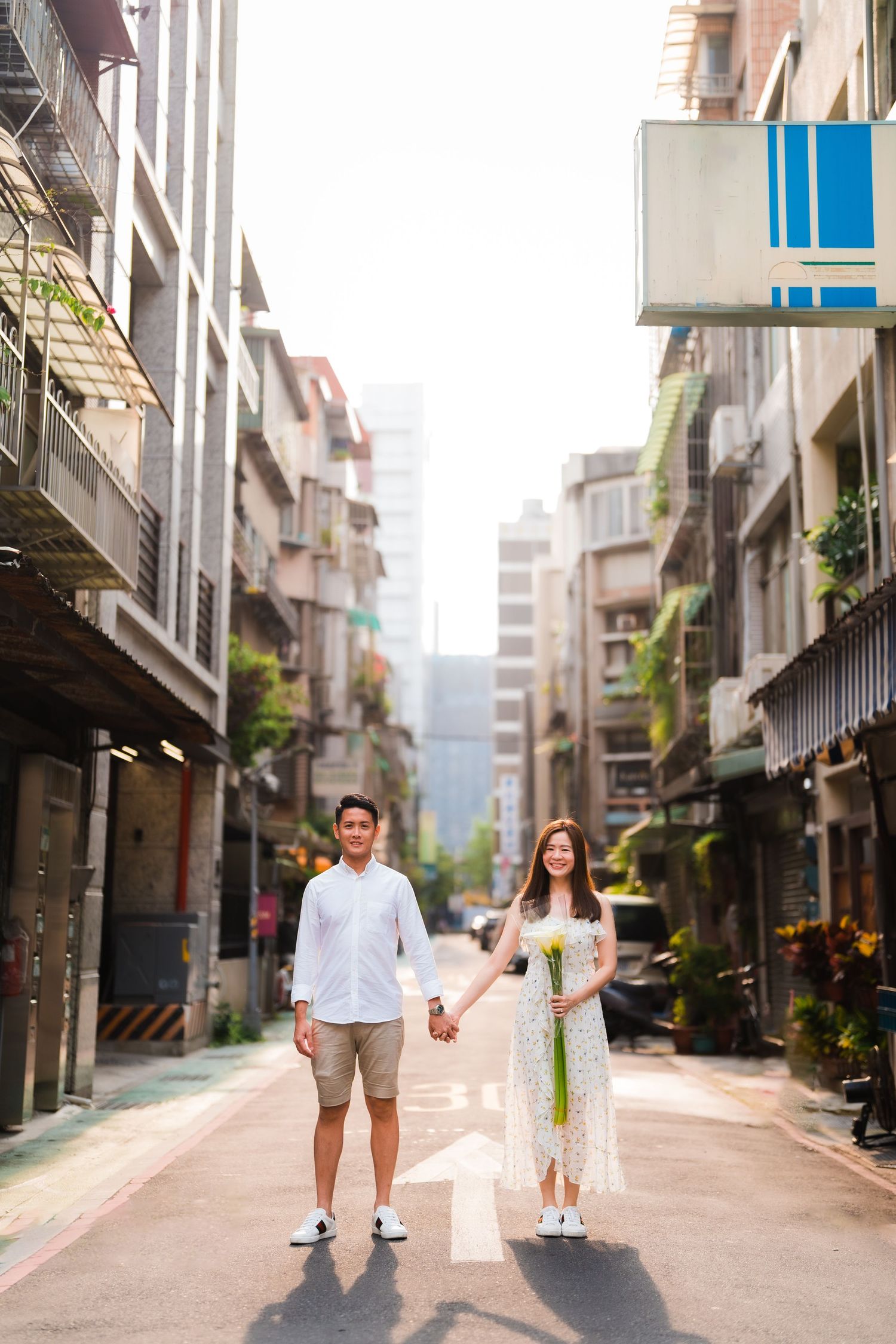Couple holding hands while walking down urban alley between apartment buildings in daylight.