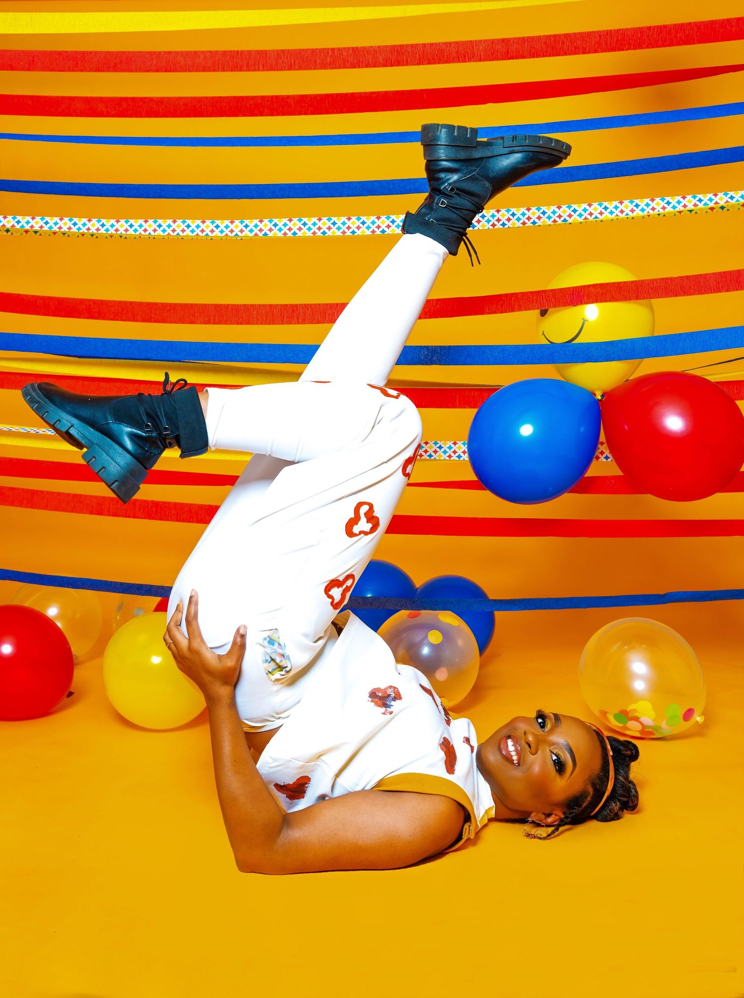 Performer in white jumpsuit does acrobatic pose against vibrant striped backdrop with red and blue balloons.