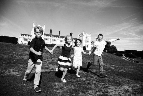 Children run and play on hill with grand castle-like building in background.