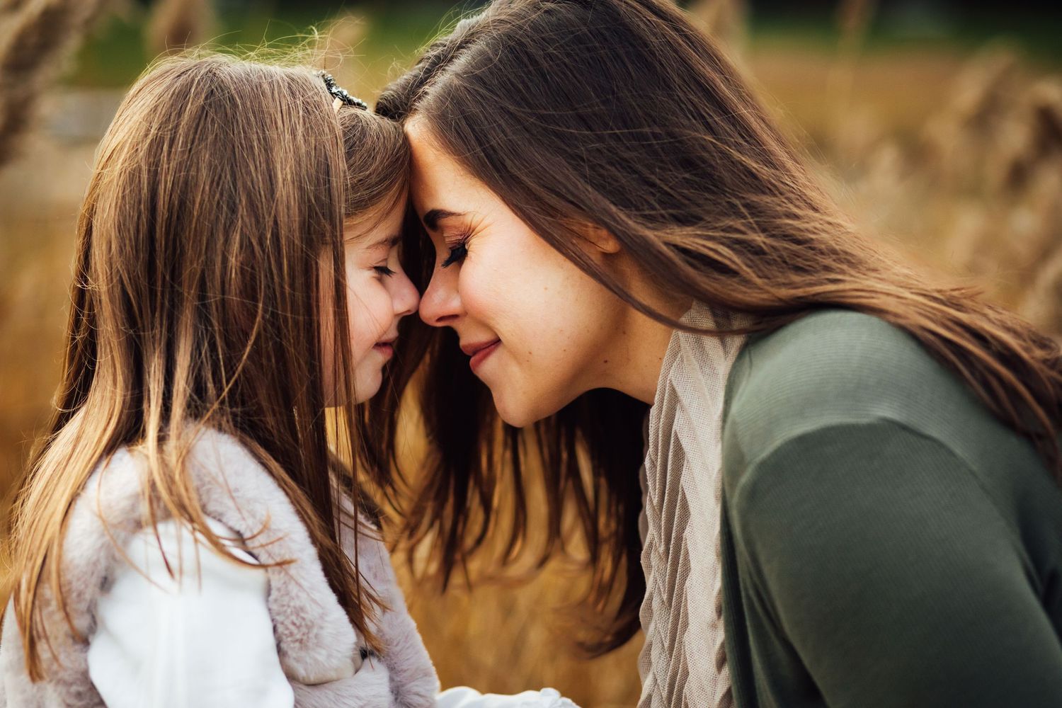 An intimate moment between parent and child touching foreheads in a golden field.