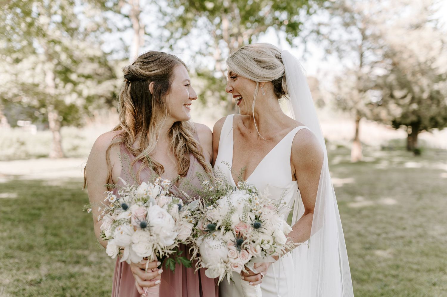 Wedding party members share joyful moments outdoors with floral bouquets.