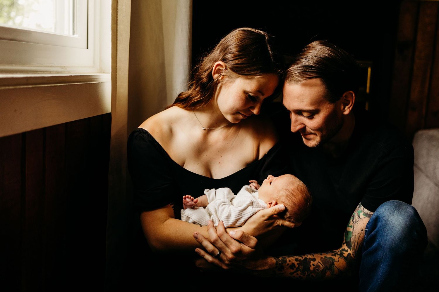 A tender family moment by window light with their newborn baby.