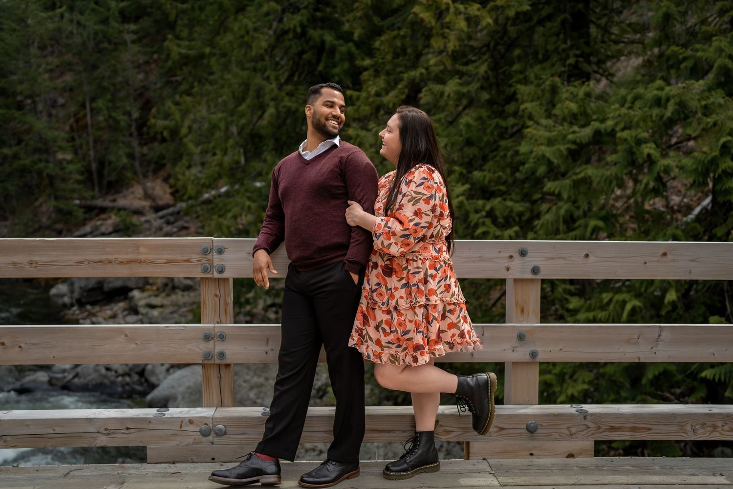 A couple sharing a playful moment on a wooden bridge in a mountain forest setting.