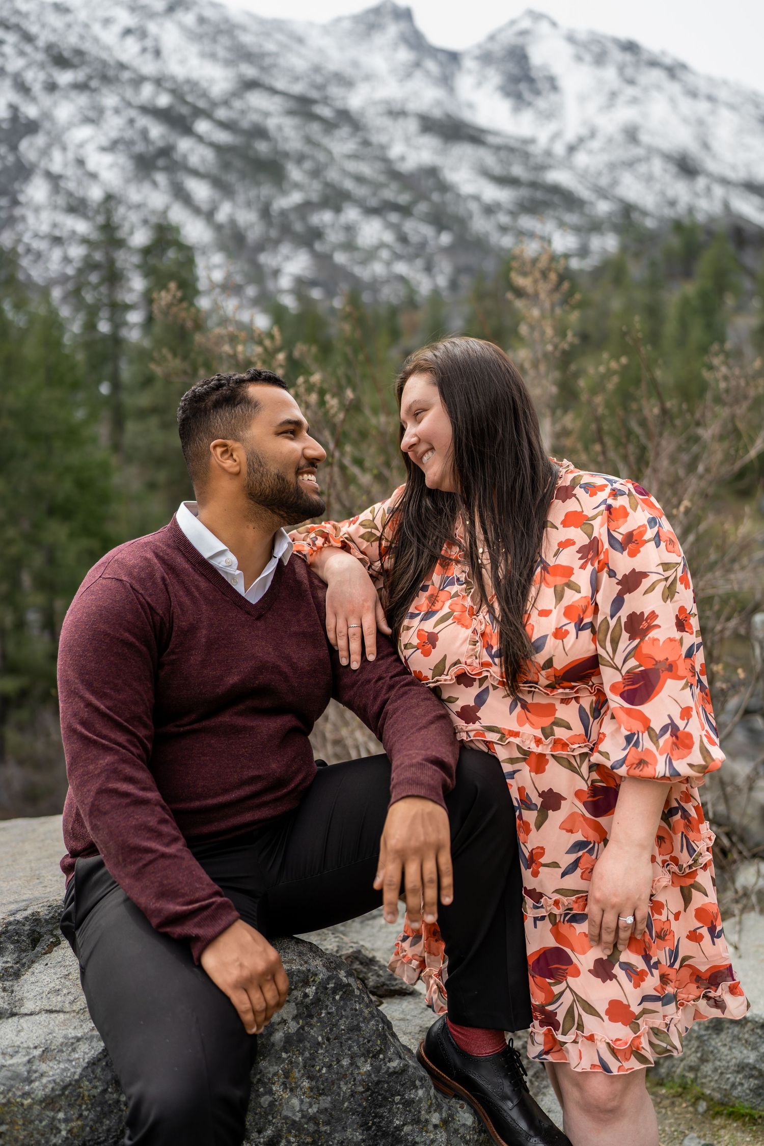 A couple enjoying a romantic moment sitting on rocks with snow-capped mountains in the background.