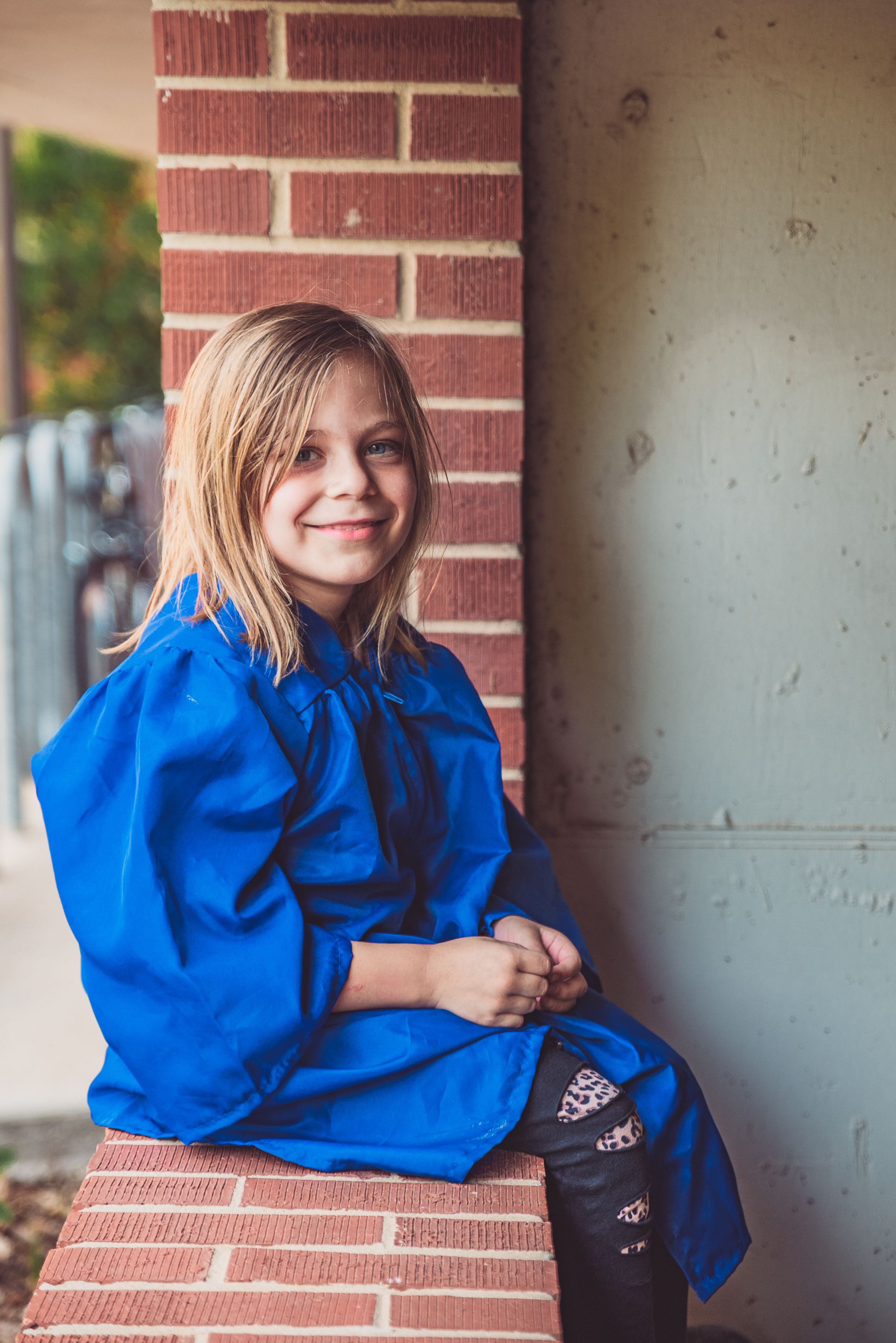 a portrait of a child sitting on a ledge in a graduation gown
