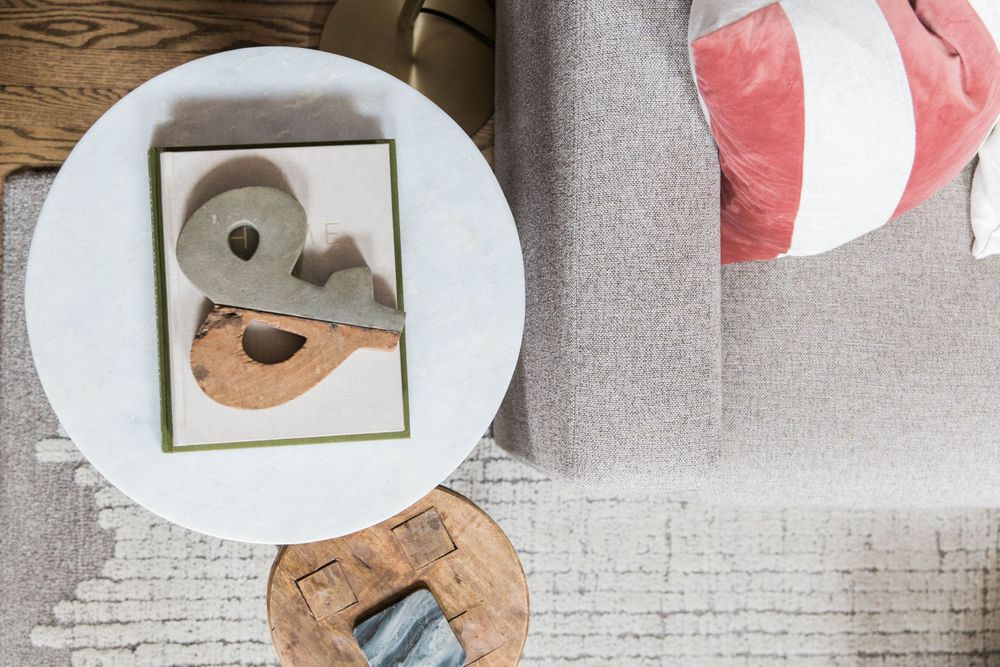 Overhead view of white round coffee table with decorative bird sculpture and pink striped pillow on gray sofa.