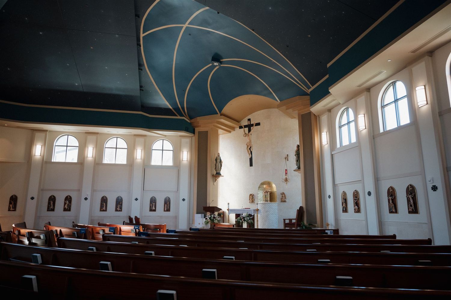 Interior of a church sanctuary with high ceilings, arched windows, and wooden pews under a dramatic blue ceiling.