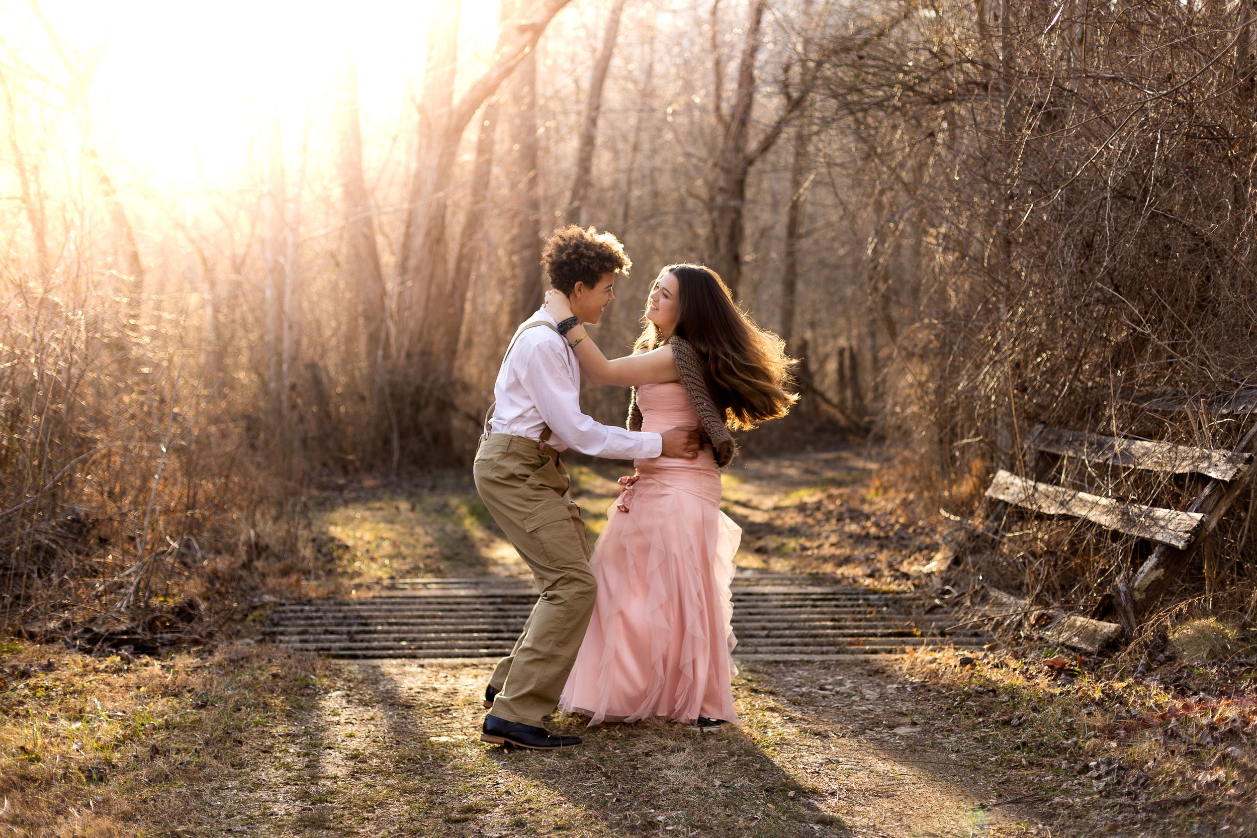 Couple dancing together on a sunlit forest path during golden hour.