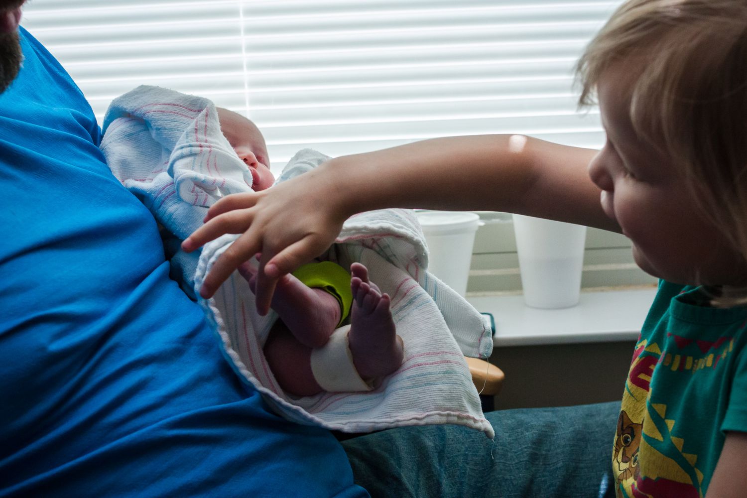 Dad holds new baby girl as his older daughter touches her sister's toes just after birth.