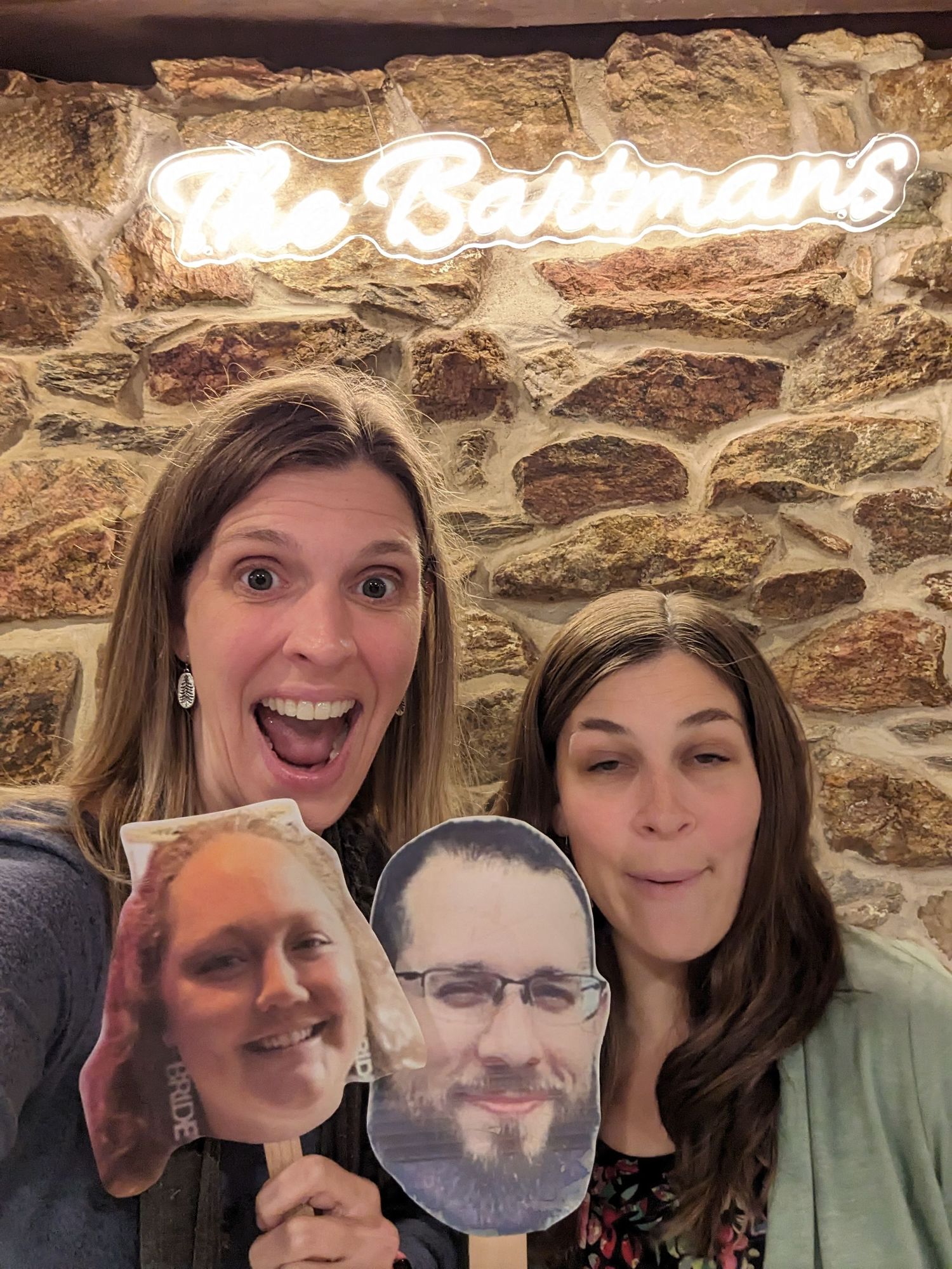 Group poses enthusiastically with a cardboard face cutout against illuminated stone wall backdrop.
