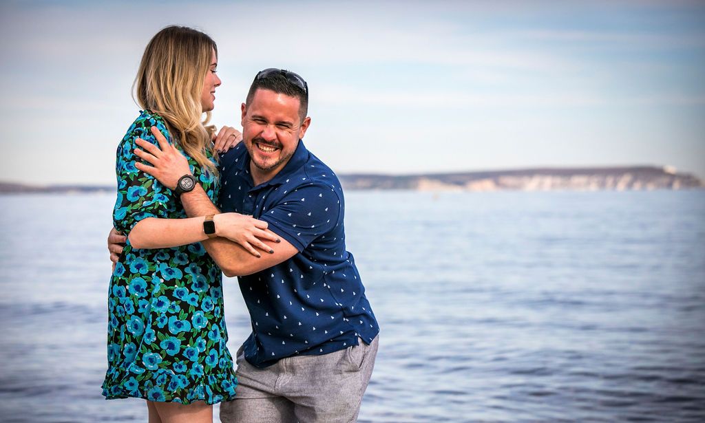 A joyful couple embraces and laughs together with ocean cliffs in the background.
