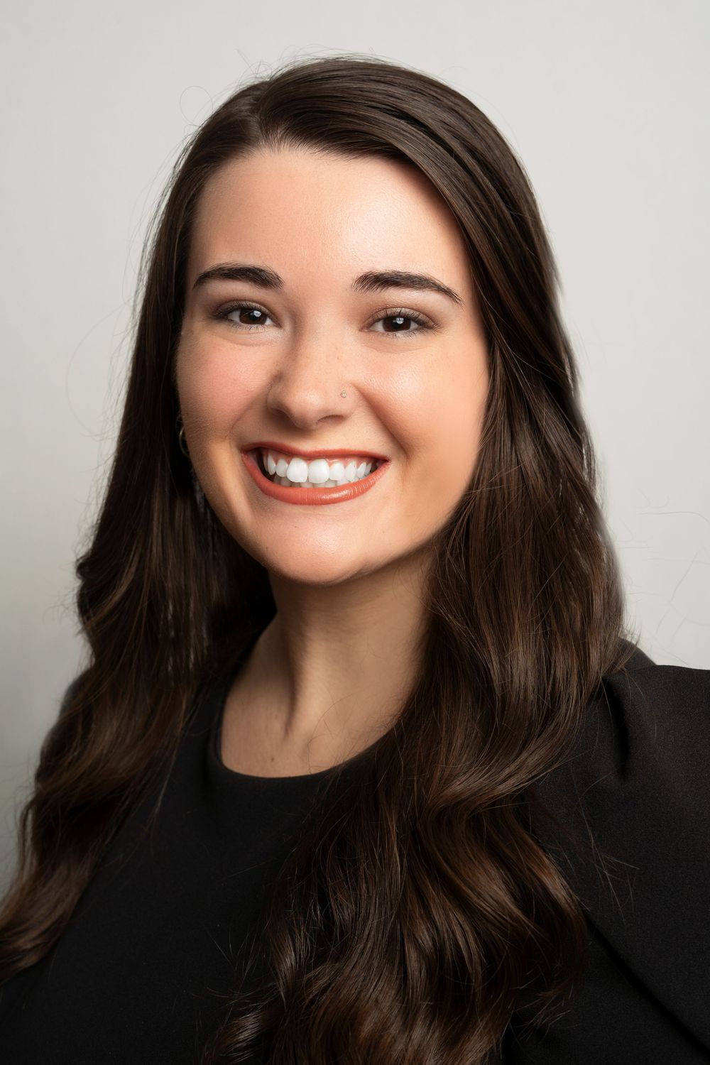 Smiling young woman with long brown hair wearing a black blazer professional headshot.