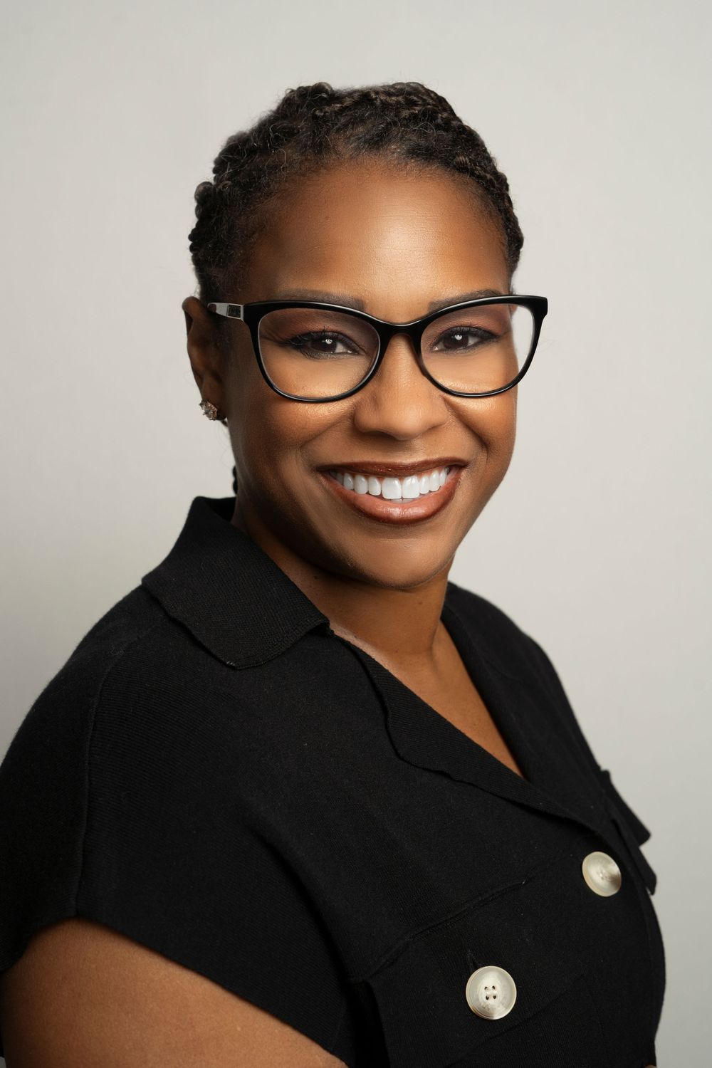 Professional Black woman with glasses and short braids wearing black top headshot.