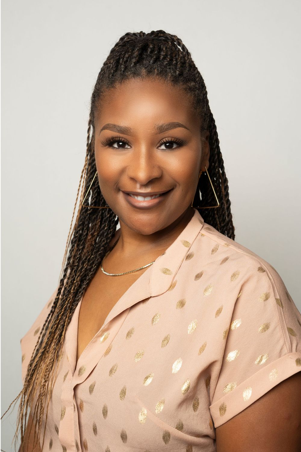 Smiling Black woman with long box braids wearing pink polka dot blouse headshot.