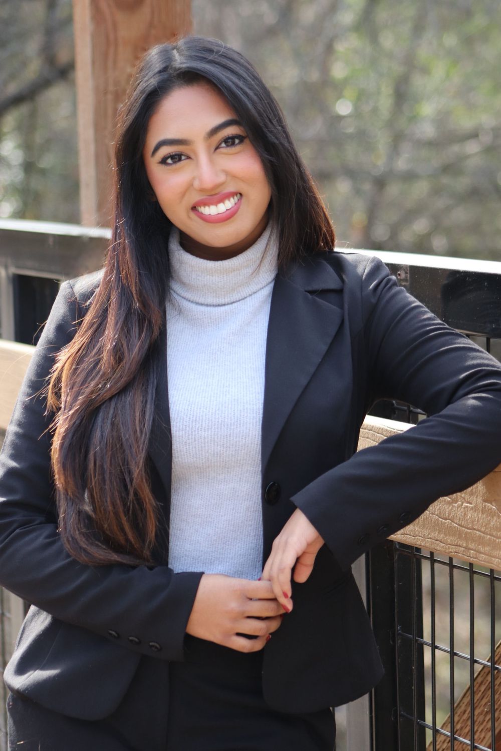 Young professional woman in black blazer and turtleneck posing confidently outdoors near a railing.