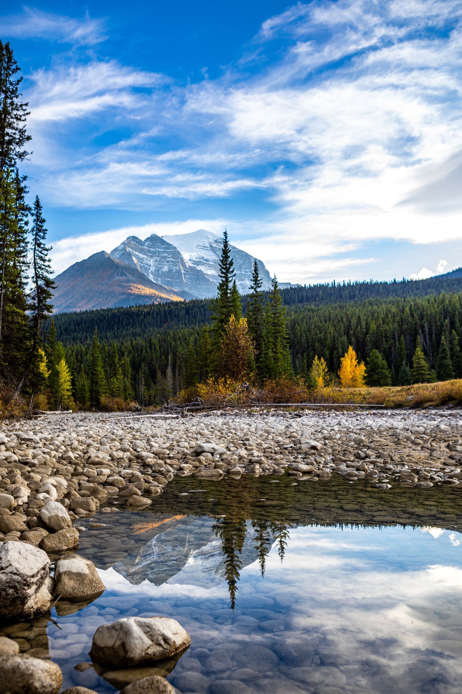 Mountain peak reflecting in rocky lake with autumn colors and blue sky in Canadian Rockies.